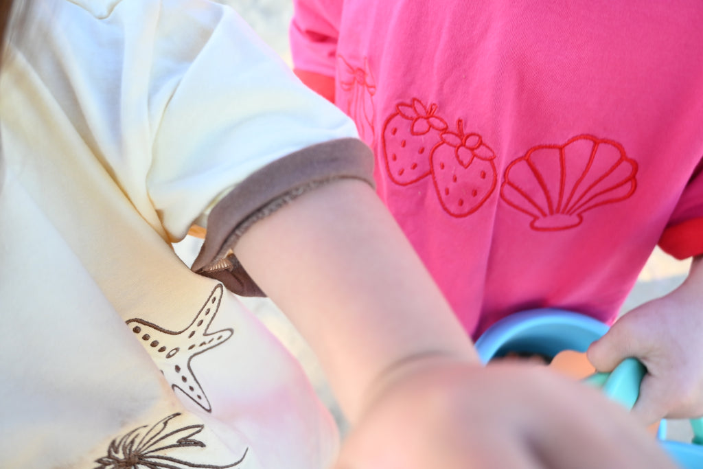 Child's arm focal point. Two children standing close to the camera. One child wearing a pink and red t-shirt and the other child wearing a beige and light brown t-shirt