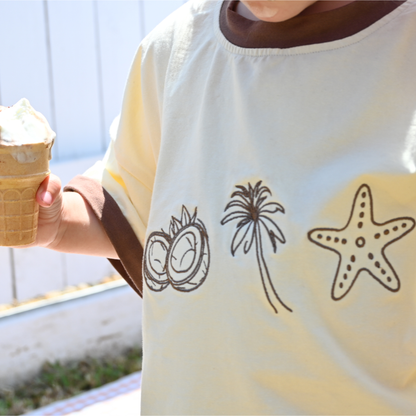 Child wearing cream shirt with coconut, palm tree, starfish designs holding melting ice cream cone
