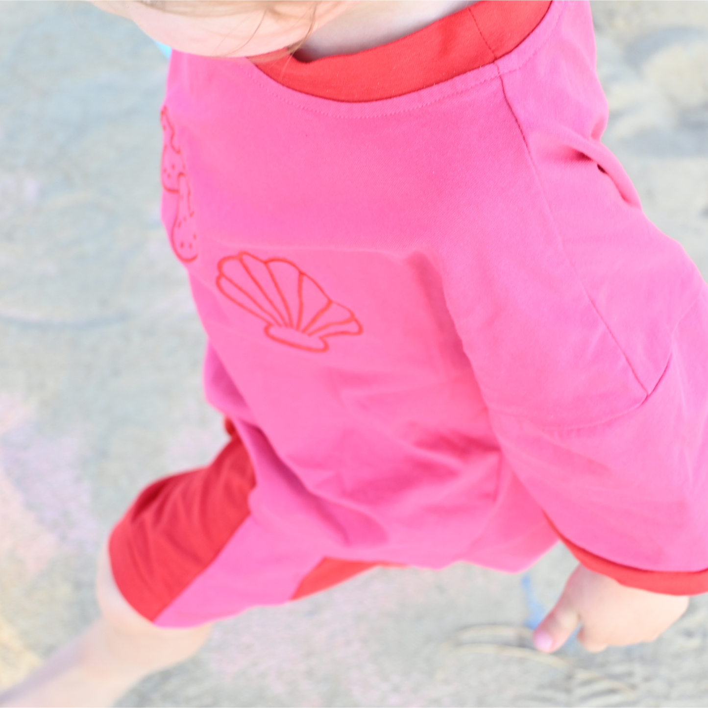 Child wearing pink and red clothing with seashell and flower prints playing on chalk-drawn pavement