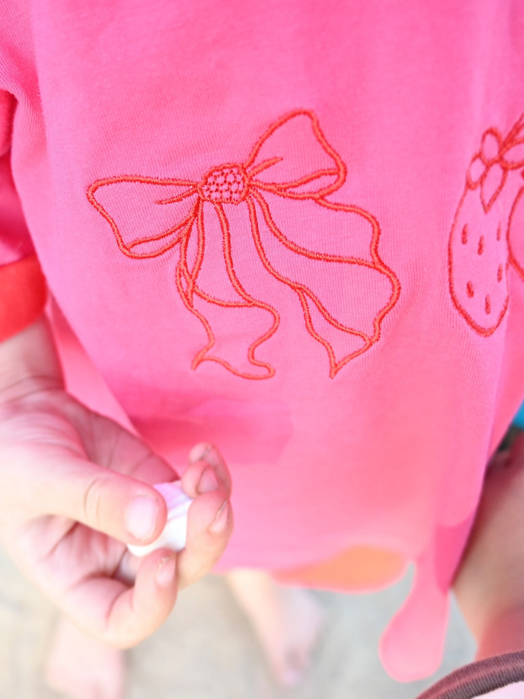 Close-up of a pink fabric with red embroidered bow design held by a hand.