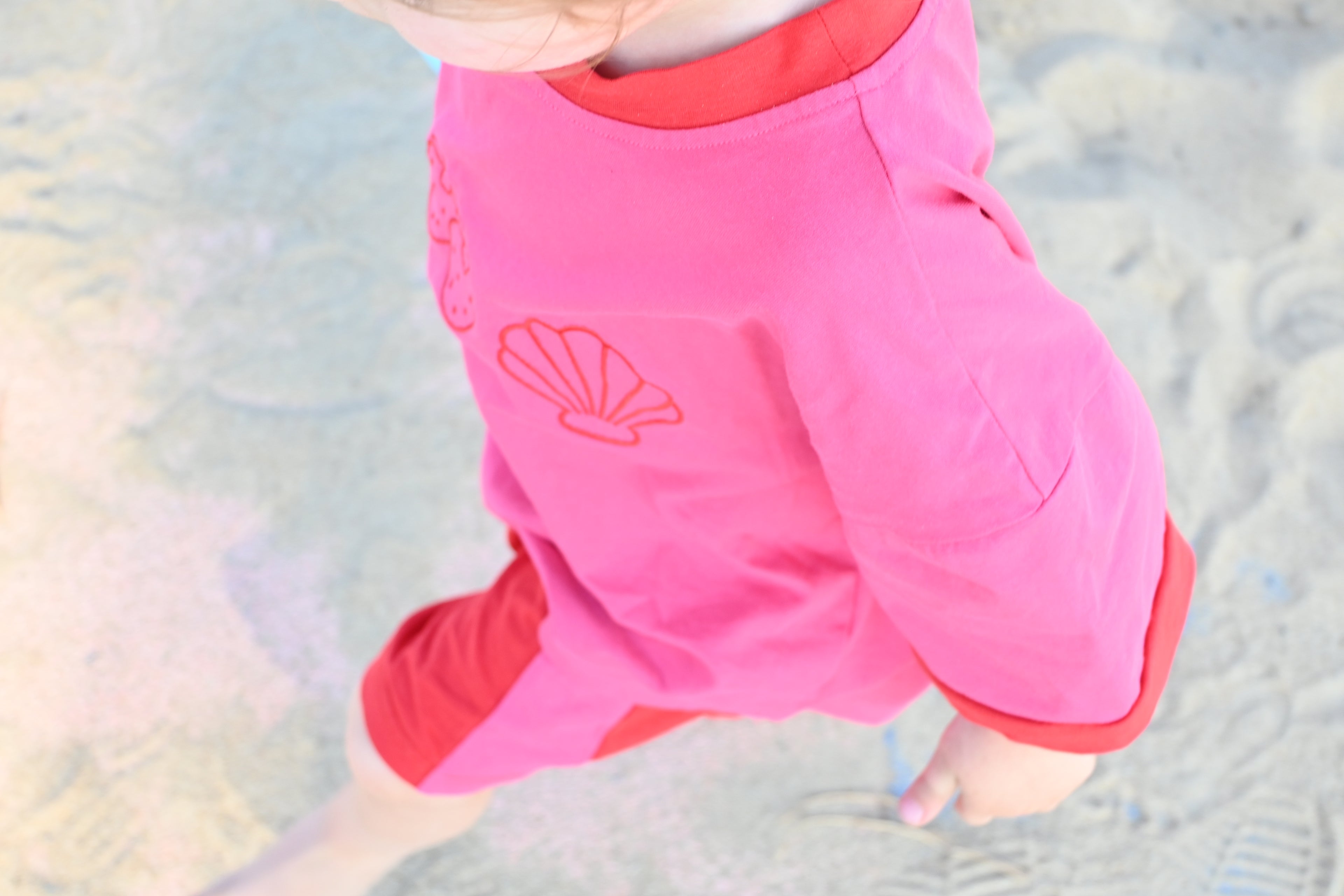 Person wearing pink shorts with a shell design on a sandy background