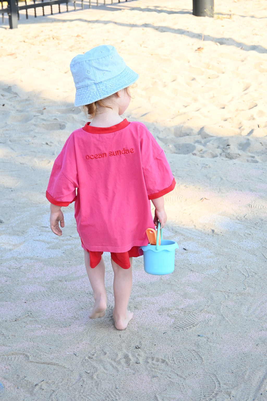 Child in a pink outfit playing on a sandy beach with sand toys.