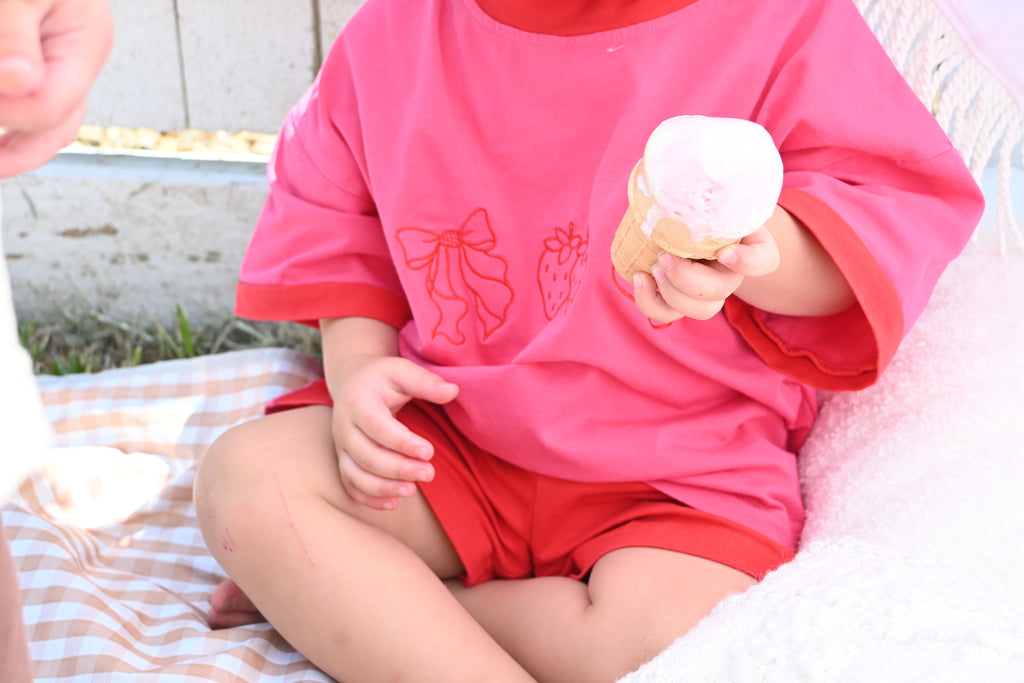 Child in pink shirt and red shorts holding a an ice cream  ball outdoors.