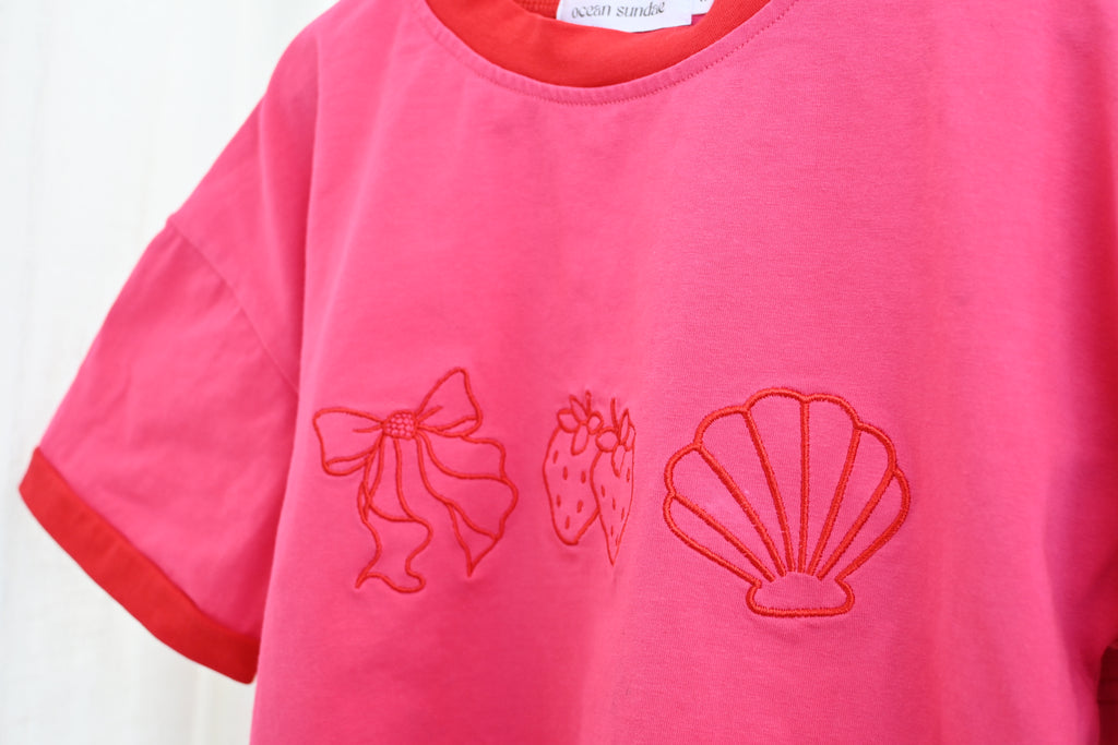 Pink shirt with red embroidered designs on a white background
