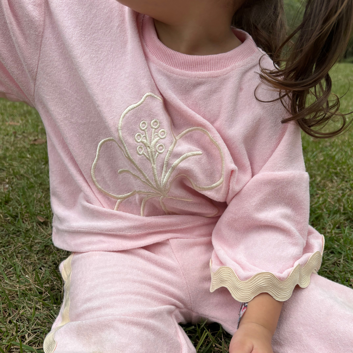 Child wearing a pink outfit with floral embroidery sitting on grass