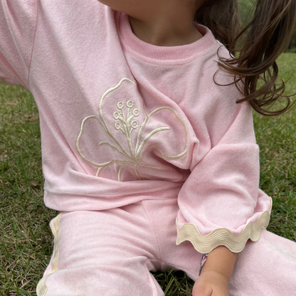 Child wearing a pink outfit with floral embroidery sitting on grass
