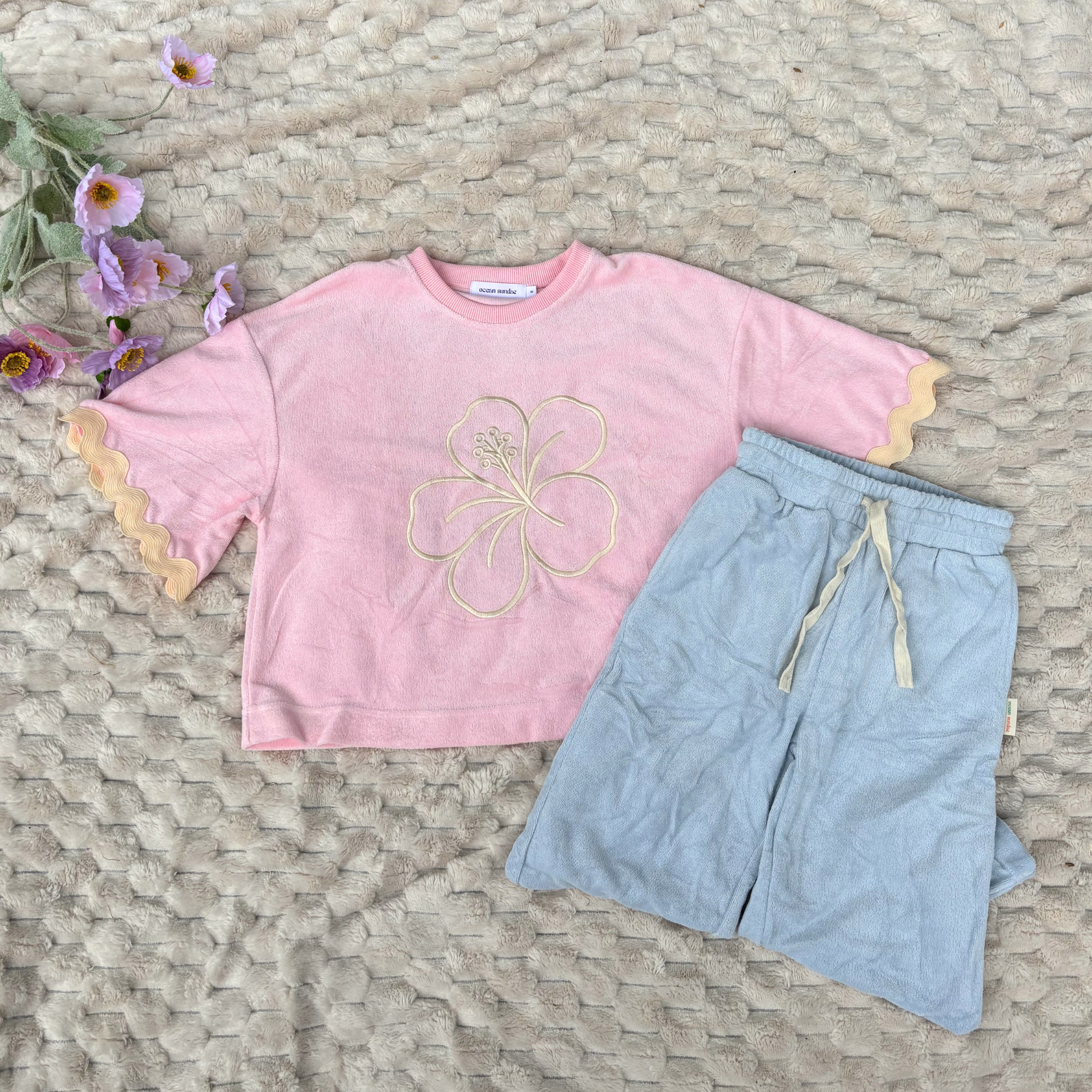 Pink shirt with floral design and light blue shorts on a textured surface with flowers.