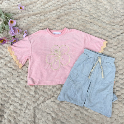 Pink shirt with floral design and light blue shorts on a textured surface with flowers.