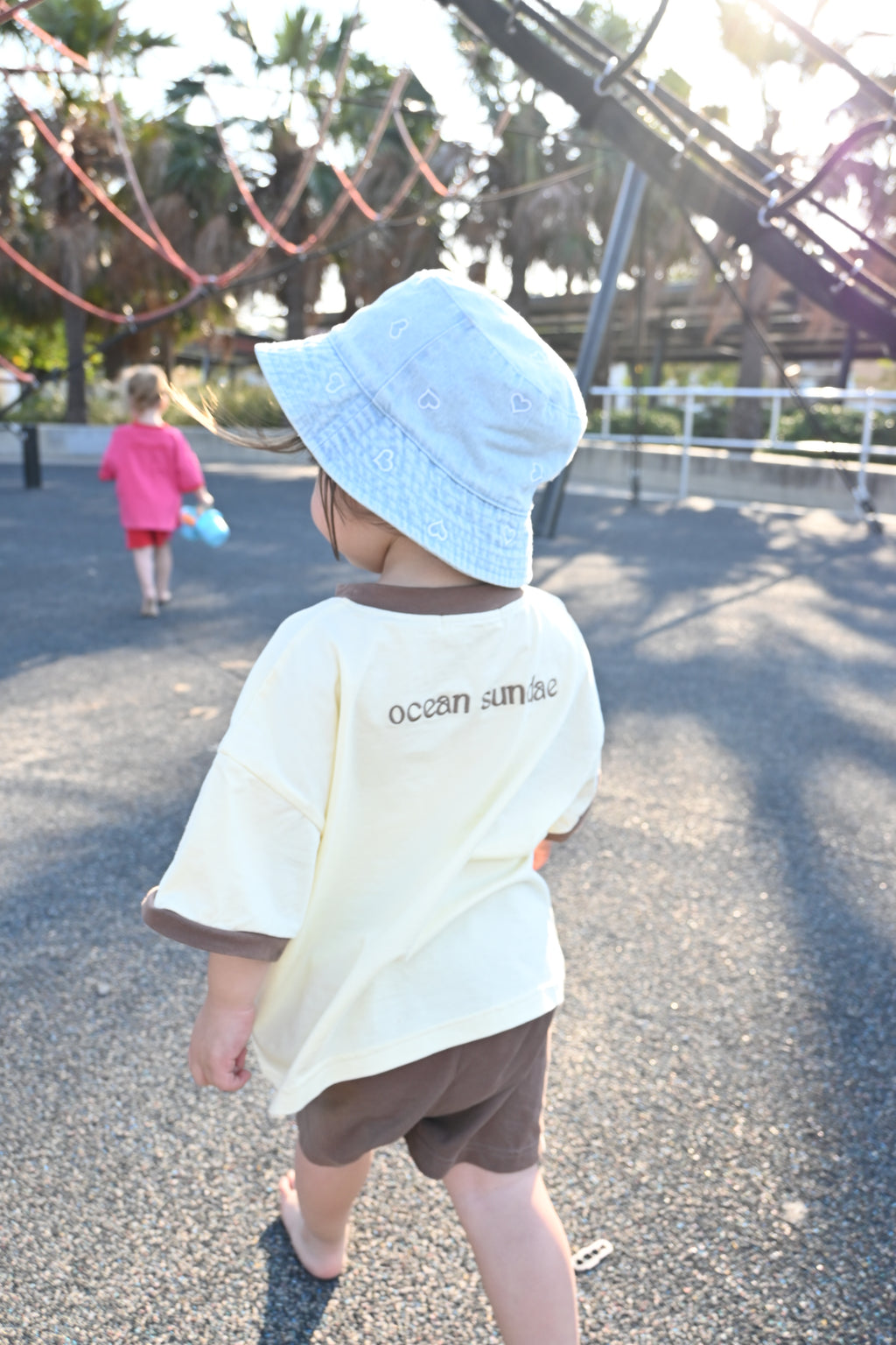 person walking in playground wearing cream shirt with brown accents and the words ocean sundae on the back of the tee