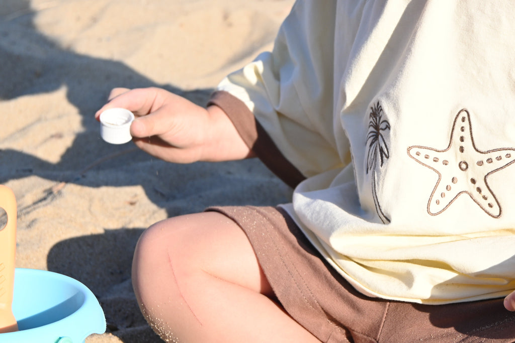 Person sitting on sand wearing a shirt with a starfish design.