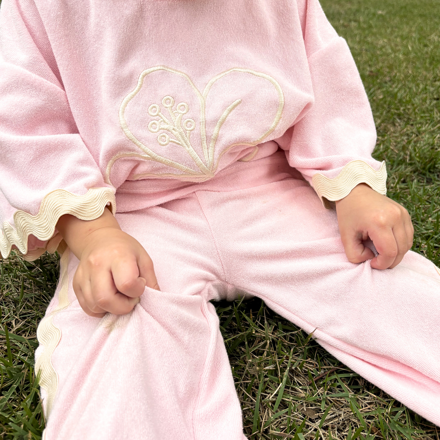 Child wearing a pink outfit with a hibiscus design sitting on grass