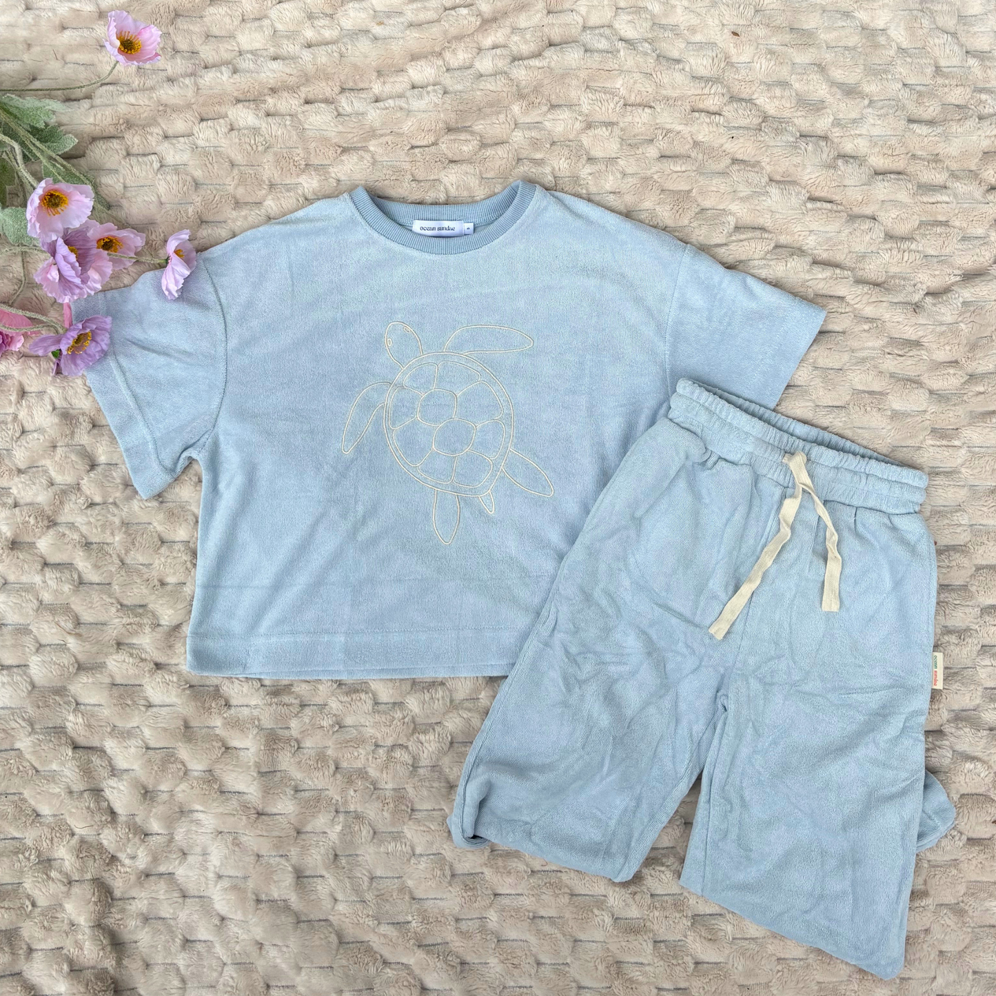 Light blue t-shirt and shorts set with a turtle design on a textured surface.