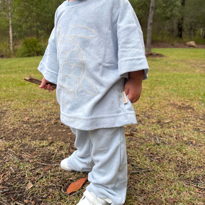 Child wearing a light blue outfit with a turtle design outdoors on a grassy area.